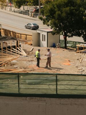Two engineers discussing plans at an active construction site under sunny skies.