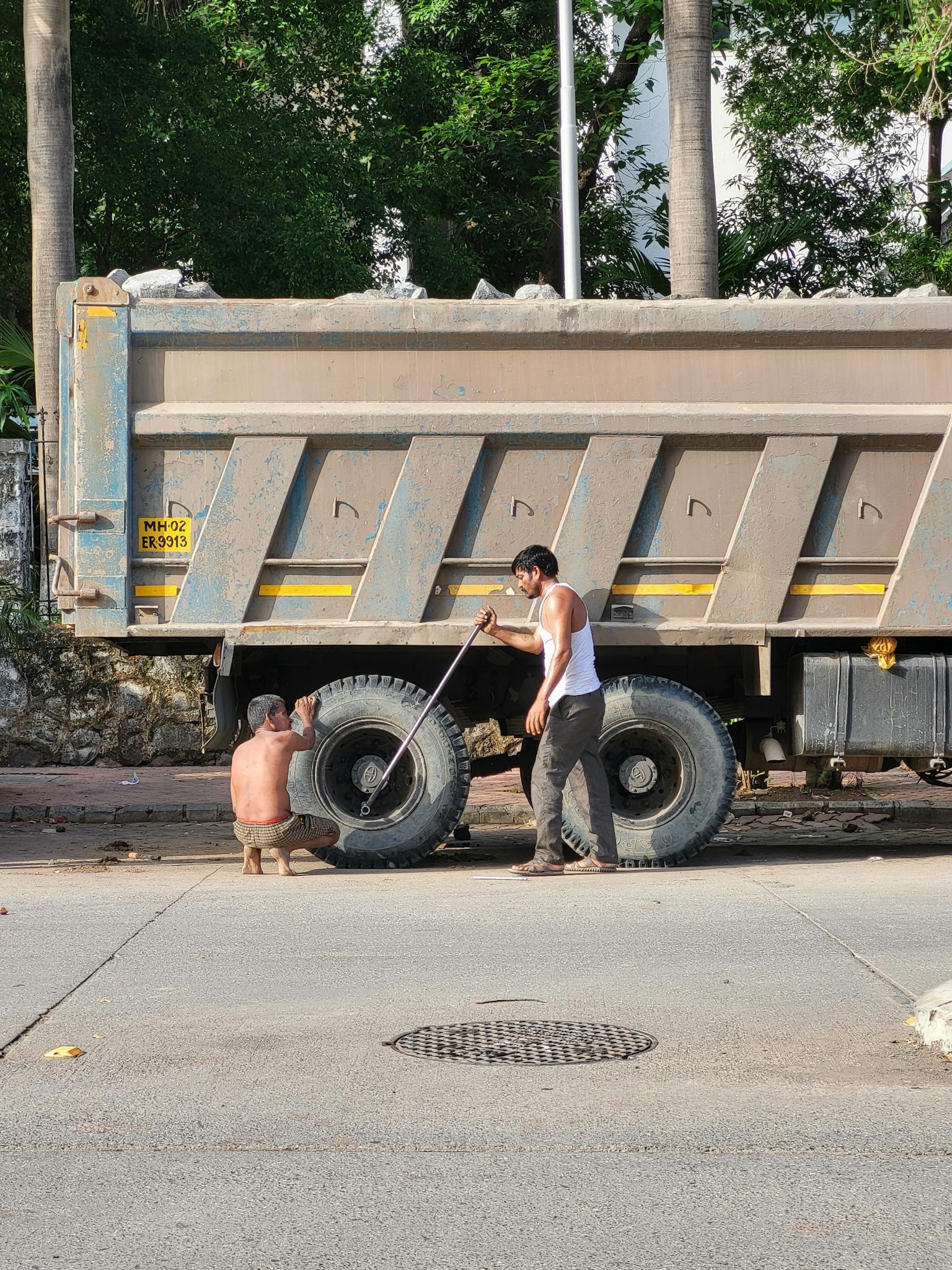Two men fixing a truck on a city street, highlighting transportation and maintenance.
